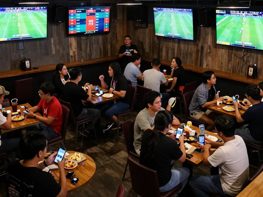 Engaged sports fans using the nhandinhkeonhacai app for betting in a lively sports bar.